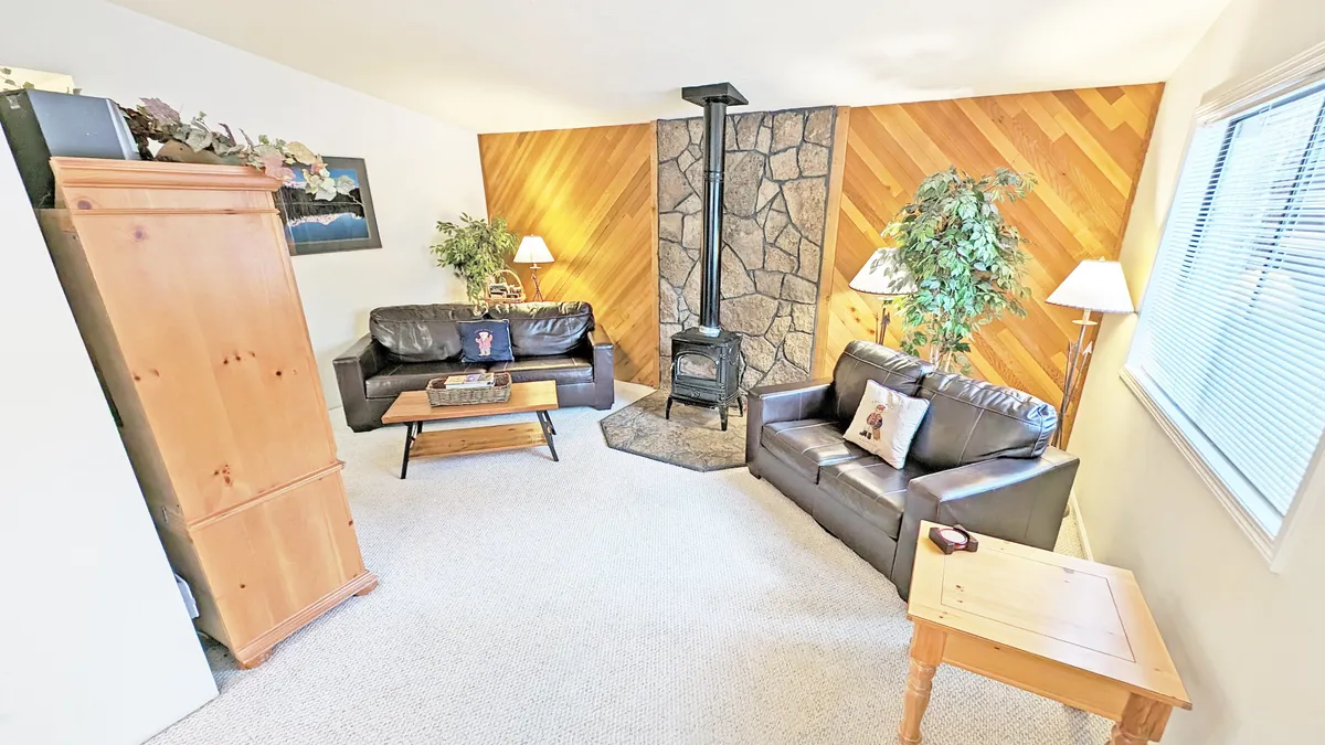 A welcoming living room with a wood-burning stove, black leather sofas, a wooden coffee table, and decorative plants. The space exudes warmth and comfort—an inviting place to relax after a day of adventure.