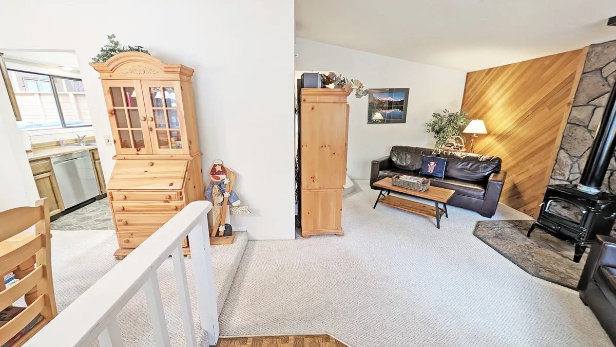 A warm, welcoming living room featuring a stone fireplace at its center, surrounded by comfortable seating, a wooden cabinet, and a large coffee table. The space is filled with rich wood accents and invites family gatherings or cozy nights by the fire.