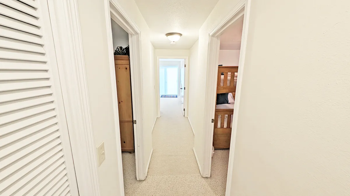 A hallway view leading to a bunk bed room, with an open doorway and a wooden dresser. The hallway feels welcoming, and the visible bedroom is ideal for families and pet lovers, hinting at inclusive accommodations.
