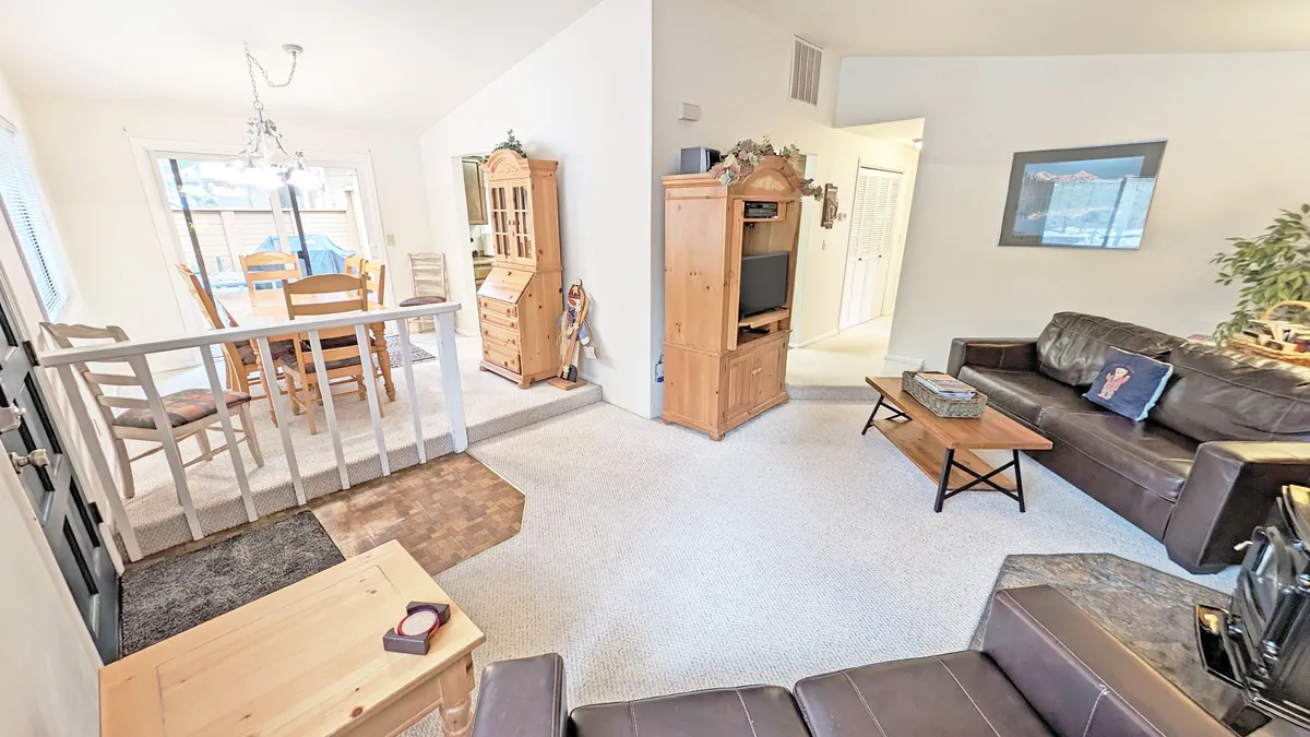 A comfortable, open-plan space showing a sofa set, a dining area, a television unit, and wooden cabinets. The scene is lit warmly, with space for family gatherings, movie nights, and intimate meals, tying together the living and dining zones.