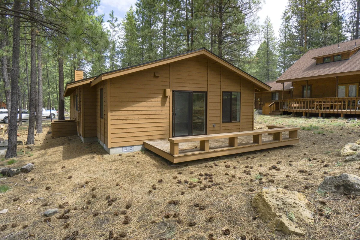 Featuring a wide wooden deck attached to the home, nestled among tall pine trees, this image provides another angle of the outdoor relaxation area. The serenity and privacy of the setting are emphasized, perfect for stargazing or soothing muscles after outdoor activities.