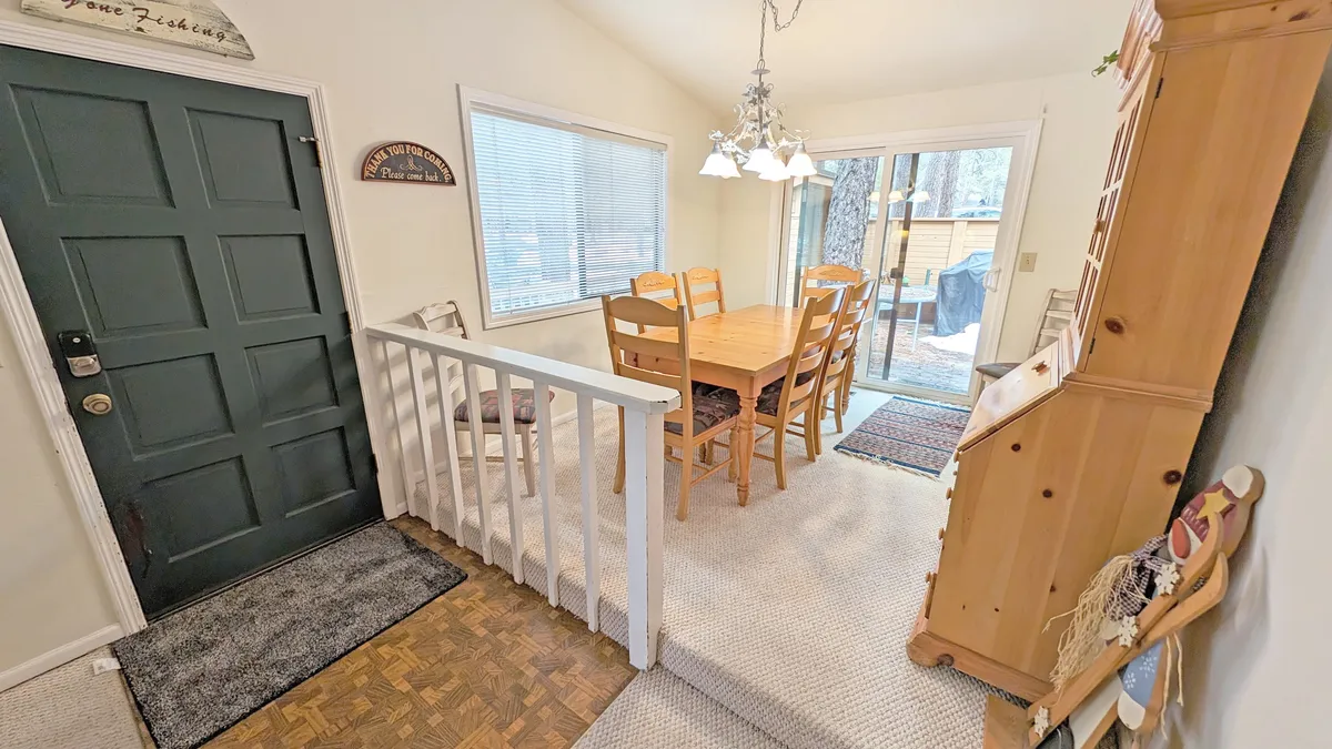 A welcoming entryway view with the front door, a dining table, large windows filling the space with light, and a wooden cabinet. The open layout hints at easy comings and goings, perfect for families heading out or returning from activities.