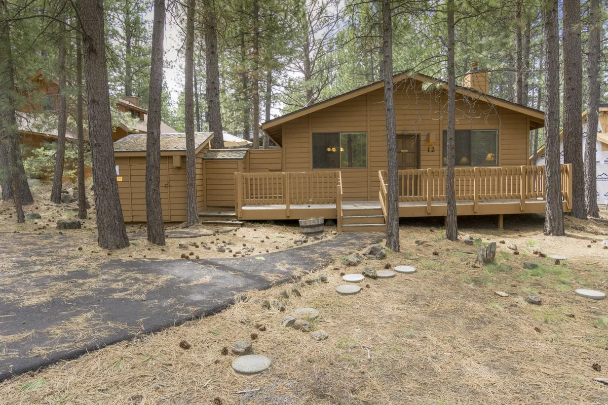 This image captures a spacious wooden deck bordered by large windows and surrounded by trees, offering a tranquil view into the natural landscape. The deck space is prominent, inviting thoughts of future outdoor relaxation, with ample room that could easily accommodate a hot tub setup.