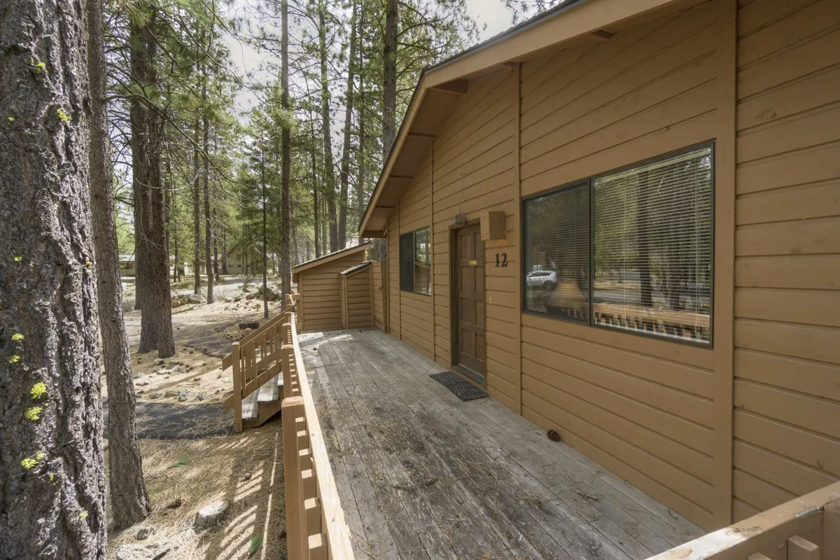 The exterior view shows Timber 12’s wooden siding, large windows, and tree-lined deck area. The natural surroundings invite families to enjoy morning coffee or evening stargazing, blending the comfort of the home with access to outdoor excitement.