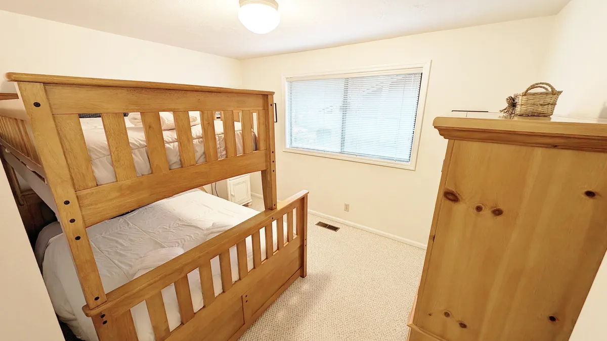 A cheerful bedroom with a sturdy pyramid-style bunk bed, a window letting in daylight, and a dresser for storage. The setup is inviting and playful, clearly designed with kids or teens in mind, offering both comfort and fun.
