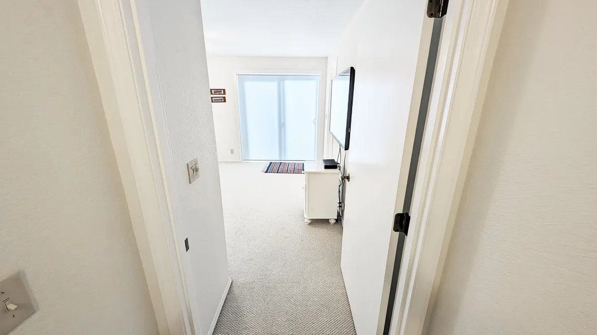 A view through a doorway leading to the living area, with sliding glass doors visible in the background. The TV sits on a small cabinet and the space feels inviting and open, connecting the interior with a sense of the outdoors.